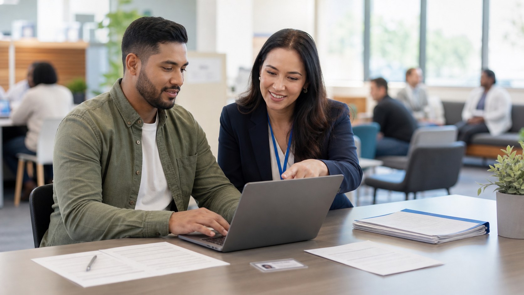 Support person helping a member use a laptop with application papers on a desk